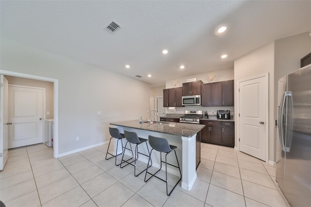 kitchen featuring appliances with stainless steel finishes, a breakfast bar, light tile patterned floors, dark brown cabinets, and a center island with sink