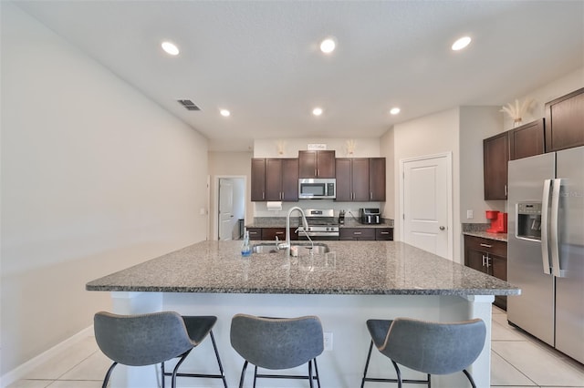 kitchen with an island with sink, sink, light tile patterned floors, dark brown cabinetry, and stainless steel appliances