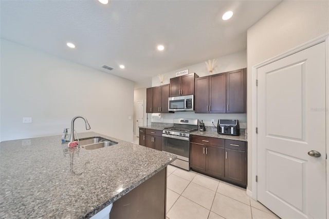 kitchen with stainless steel appliances, dark stone countertops, light tile patterned floors, sink, and dark brown cabinetry