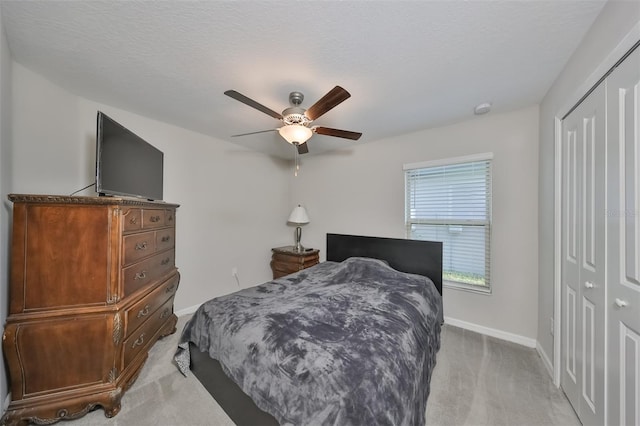 bedroom featuring ceiling fan, light colored carpet, a closet, and a textured ceiling