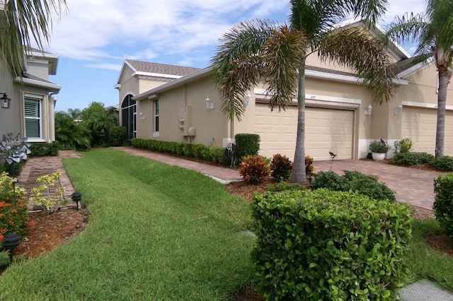 view of property exterior featuring decorative driveway, a yard, an attached garage, and stucco siding