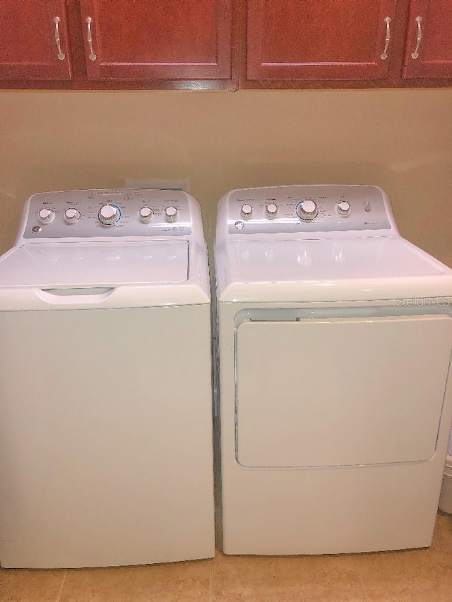 washroom with light tile patterned floors, cabinets, and washer and dryer