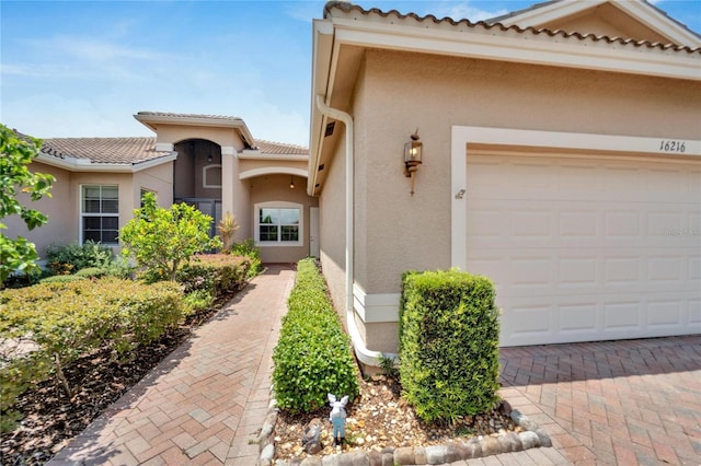 property entrance featuring a garage, a tiled roof, and stucco siding