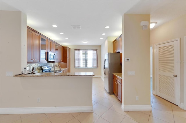 kitchen featuring stainless steel appliances, a peninsula, visible vents, brown cabinets, and decorative backsplash