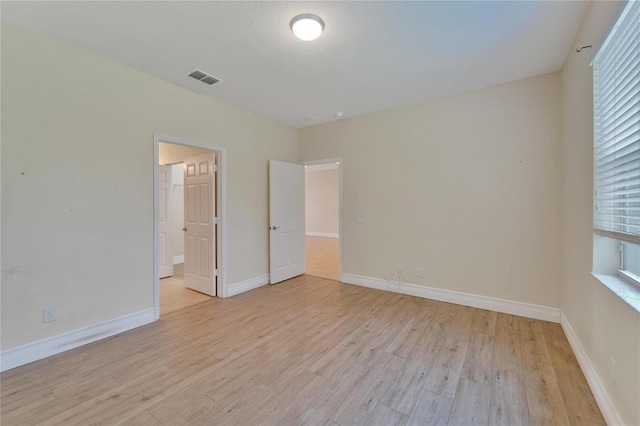 unfurnished bedroom featuring ensuite bath, light wood-style flooring, visible vents, and baseboards