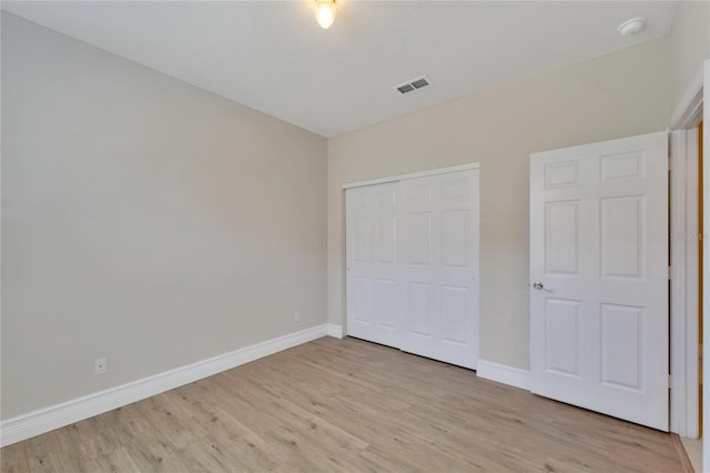 unfurnished bedroom featuring light wood-style floors, baseboards, visible vents, and a closet