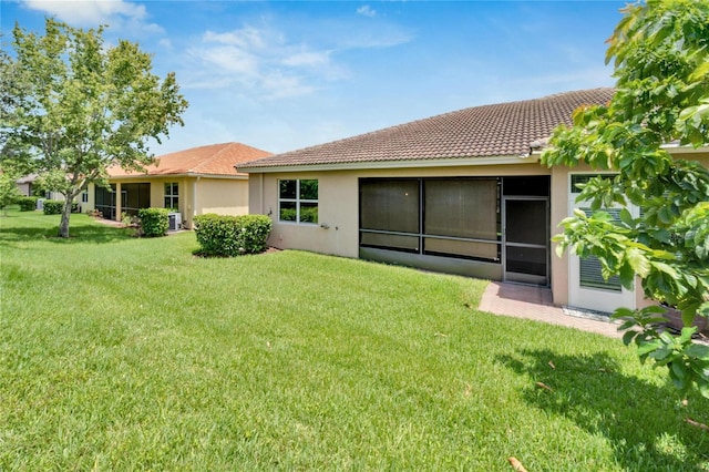 rear view of property featuring a tile roof, a lawn, and stucco siding