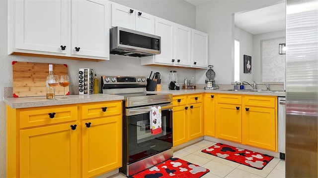 kitchen with appliances with stainless steel finishes, light tile patterned flooring, white cabinets, and sink