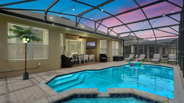 pool at dusk with ceiling fan, a lanai, and a patio area