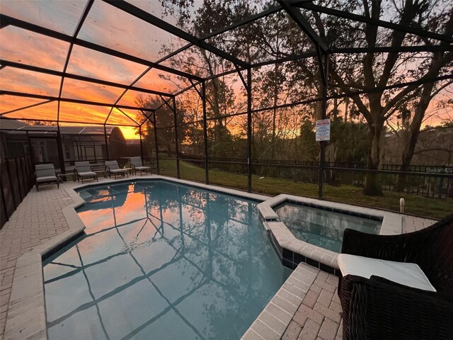 pool at dusk featuring glass enclosure, an in ground hot tub, and a patio area