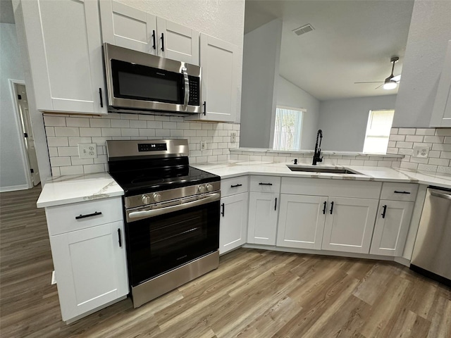 kitchen with appliances with stainless steel finishes, light wood-type flooring, sink, and lofted ceiling