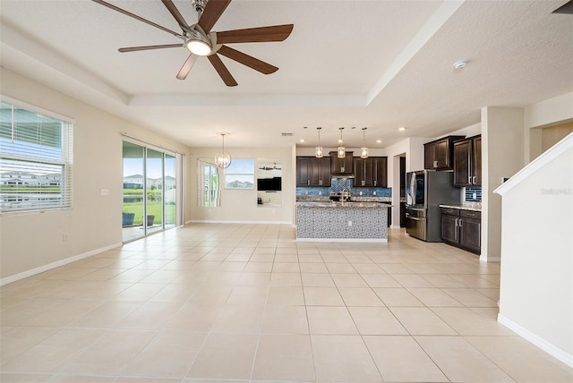 unfurnished living room featuring a tray ceiling, baseboards, and light tile patterned floors