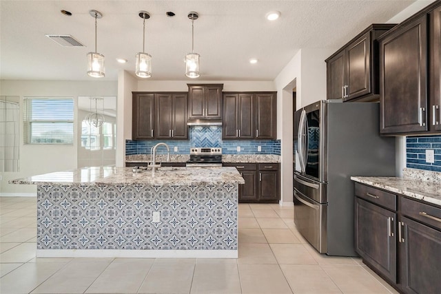 kitchen with visible vents, dark brown cabinets, appliances with stainless steel finishes, an island with sink, and decorative light fixtures