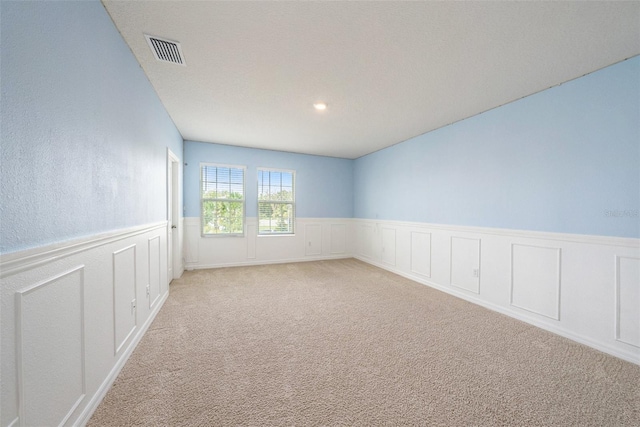 unfurnished room with light carpet, a wainscoted wall, and visible vents