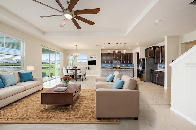 living area with recessed lighting, a tray ceiling, light tile patterned flooring, baseboards, and ceiling fan with notable chandelier