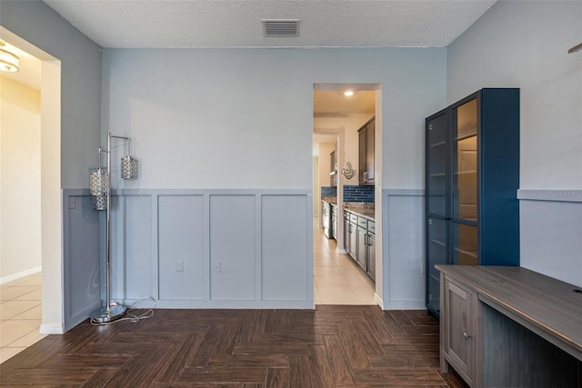 kitchen with wainscoting, glass insert cabinets, visible vents, and a decorative wall