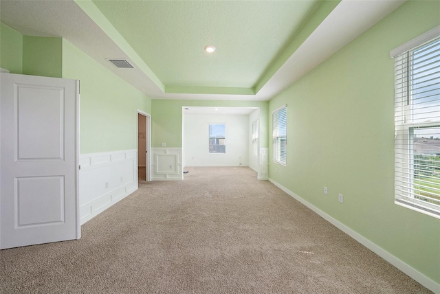 empty room with a raised ceiling, visible vents, plenty of natural light, and light carpet