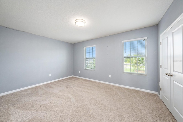 unfurnished room with carpet, plenty of natural light, a textured ceiling, and baseboards