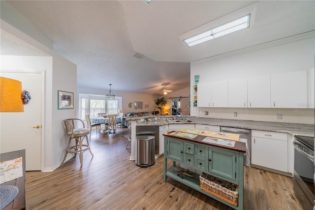 kitchen featuring a breakfast bar area, appliances with stainless steel finishes, light hardwood / wood-style floors, vaulted ceiling with skylight, and kitchen peninsula