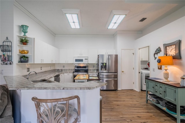 kitchen with appliances with stainless steel finishes, tasteful backsplash, washer / clothes dryer, light hardwood / wood-style floors, and kitchen peninsula