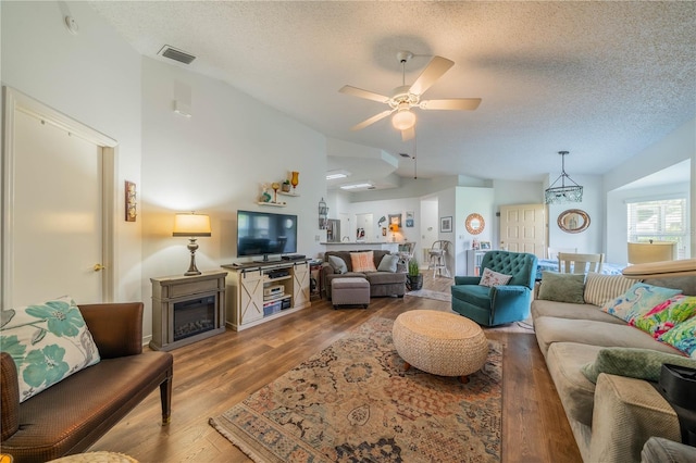 living room with ceiling fan, hardwood / wood-style flooring, a textured ceiling, and vaulted ceiling