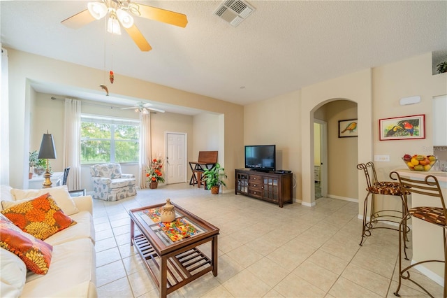 living area featuring arched walkways, light tile patterned floors, a textured ceiling, and visible vents