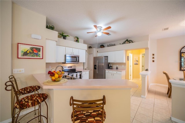 kitchen with light tile patterned floors, a peninsula, appliances with stainless steel finishes, and a kitchen breakfast bar