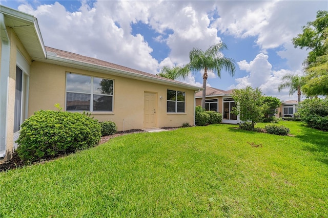 rear view of property featuring a lawn and stucco siding