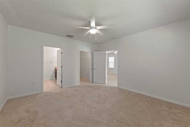 unfurnished bedroom with ceiling fan, a spacious closet, ensuite bath, and light carpet