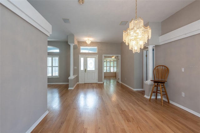 entryway featuring decorative columns, light hardwood / wood-style floors, and a notable chandelier