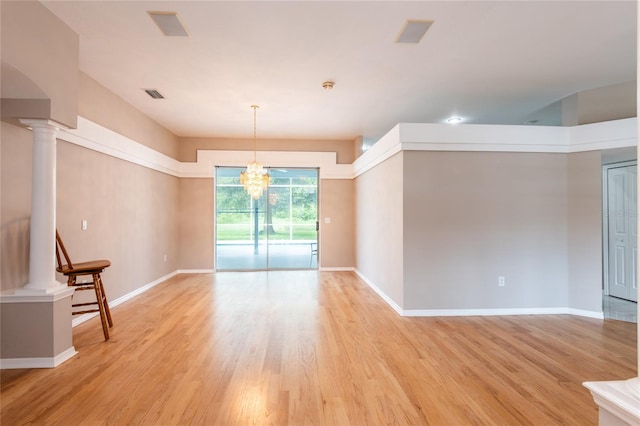 empty room featuring light wood-type flooring, decorative columns, and an inviting chandelier