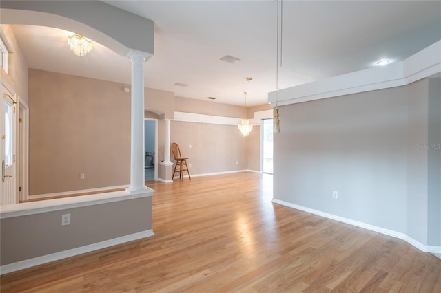 unfurnished room with an inviting chandelier, decorative columns, and light hardwood / wood-style flooring