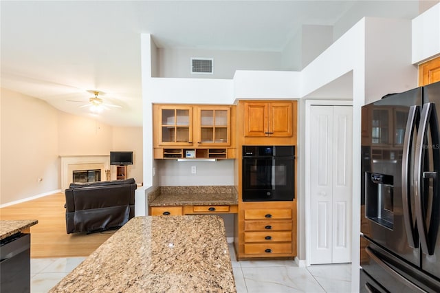 kitchen featuring light stone countertops, ceiling fan, and black appliances