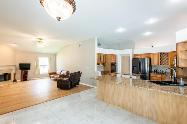 kitchen featuring kitchen peninsula, appliances with stainless steel finishes, light stone counters, ceiling fan, and sink