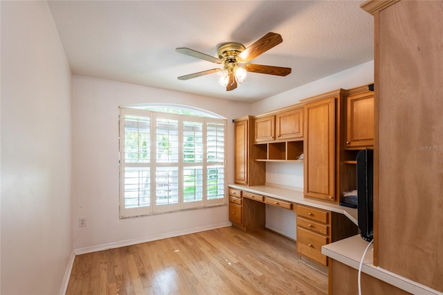 unfurnished office featuring ceiling fan, built in desk, and light hardwood / wood-style flooring