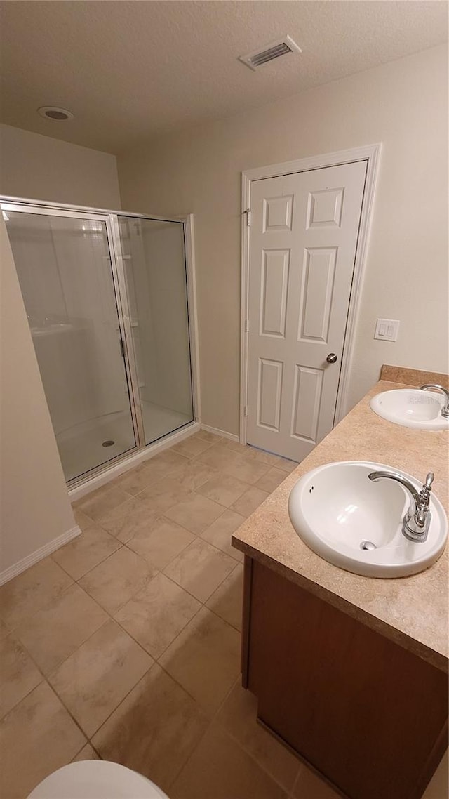 bathroom featuring a shower with shower door, tile patterned floors, and dual bowl vanity