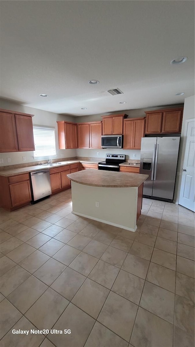 kitchen with stainless steel appliances, sink, a kitchen island, and light tile patterned floors