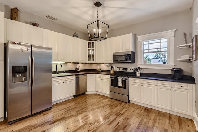 kitchen with stainless steel appliances, pendant lighting, a notable chandelier, white cabinetry, and light hardwood / wood-style flooring