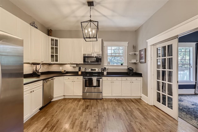 kitchen featuring white cabinets, stainless steel appliances, hanging light fixtures, and light hardwood / wood-style floors