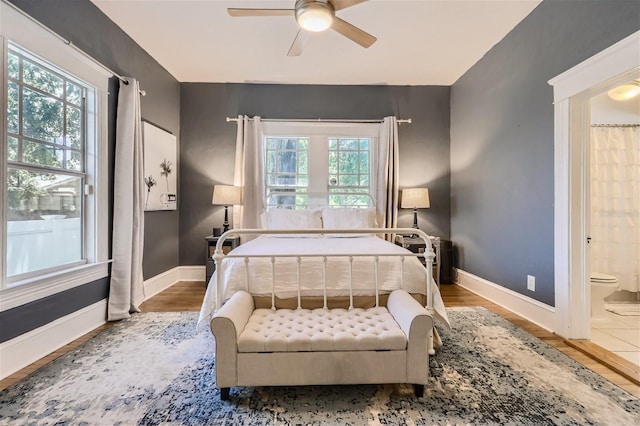 bedroom featuring ensuite bath, ceiling fan, hardwood / wood-style flooring, and multiple windows