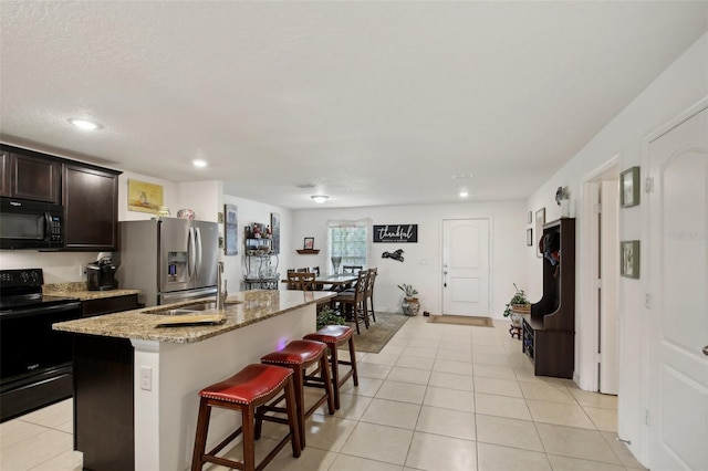 kitchen with a kitchen breakfast bar, light stone counters, sink, black appliances, and a center island with sink