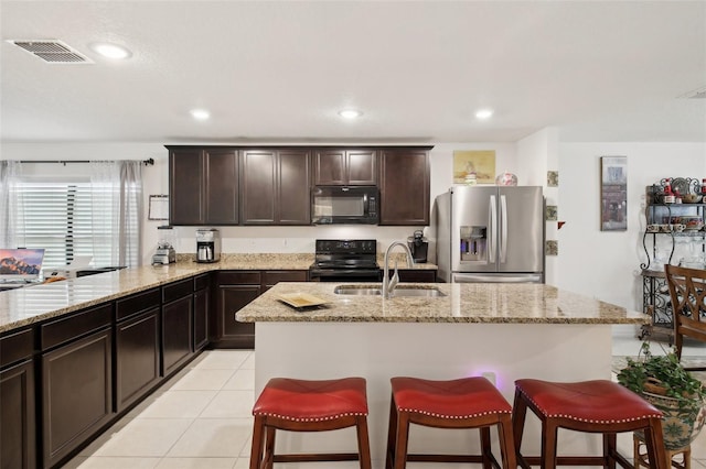 kitchen featuring stainless steel fridge, range with electric cooktop, light stone countertops, light tile patterned floors, and a center island with sink