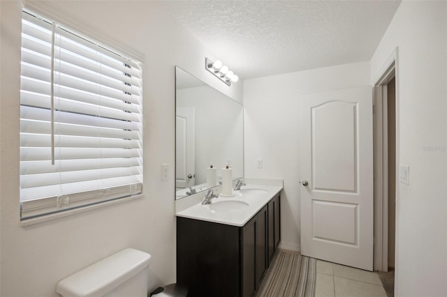 bathroom featuring toilet, dual bowl vanity, tile patterned flooring, and a textured ceiling