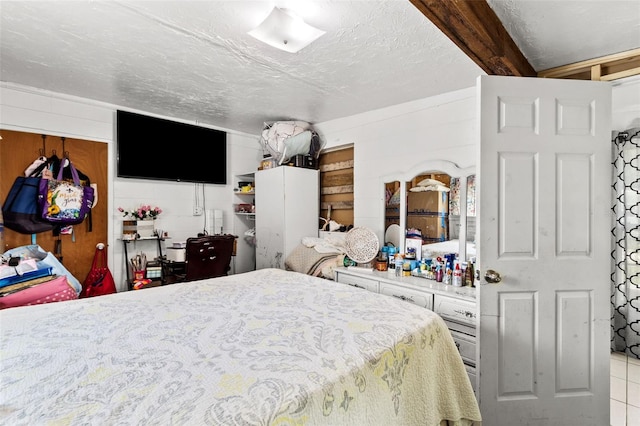 bedroom featuring wood walls, light tile patterned floors, beamed ceiling, and a textured ceiling