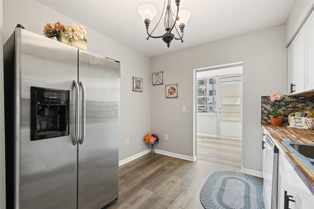 kitchen with appliances with stainless steel finishes, white cabinetry, decorative backsplash, hardwood / wood-style floors, and decorative light fixtures