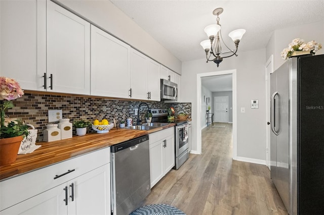 kitchen with hanging light fixtures, decorative backsplash, appliances with stainless steel finishes, sink, and light hardwood / wood-style floors