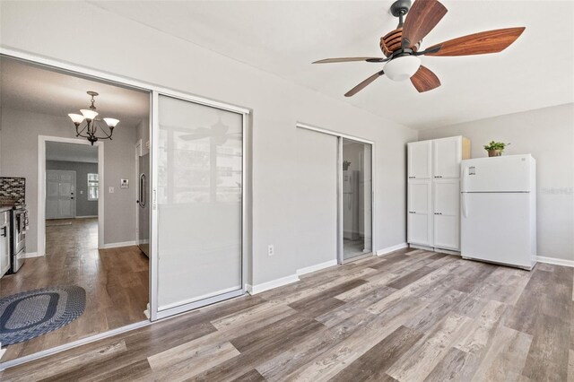 unfurnished bedroom with connected bathroom, ceiling fan with notable chandelier, white refrigerator, stainless steel refrigerator, and hardwood / wood-style flooring