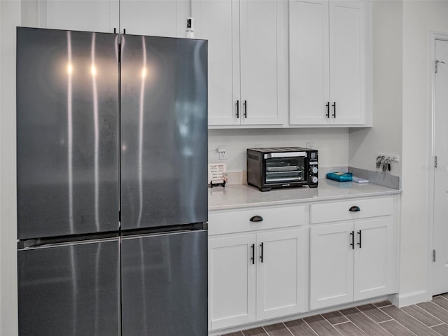 kitchen with wood tiled floor, a toaster, white cabinets, and freestanding refrigerator