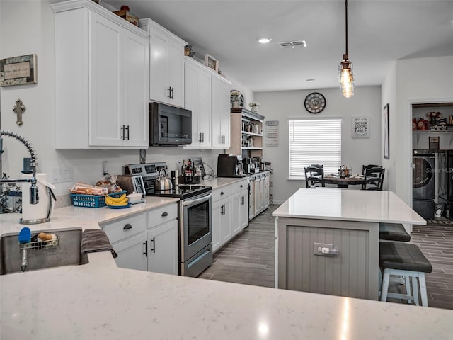 kitchen with a breakfast bar area, electric range, wood tiled floor, a kitchen island, and black microwave