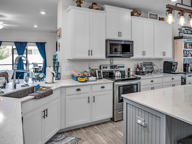 kitchen with wood finish floors, electric stove, white cabinetry, a sink, and light stone countertops